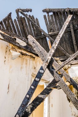The remains of the burnt house. Ruined and collapsed house burnt and damaged in the fire with remains of the wooden reinforcement poles of roof selective focus. Burned house