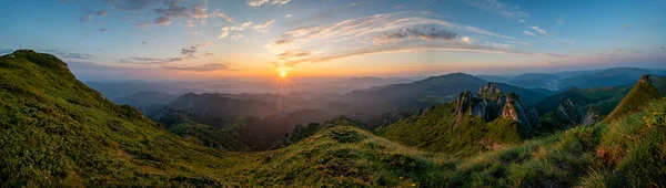 Panorama of green meadow with rocks and rocky mountains in romanian mountains in muntii ciucas with raising sun