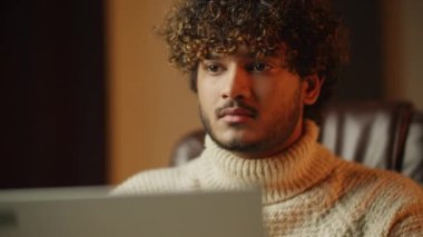 Selective focus of focused curly young man working with computer. Concentrated student using laptop on blurred background. Online studying. High quality 4k footage