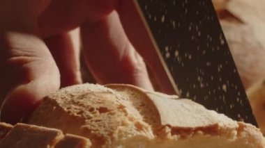 Man cutting a piece of fresh bread during dinner. Close up view of a person slicing baguette with a knife. High quality 4k footage