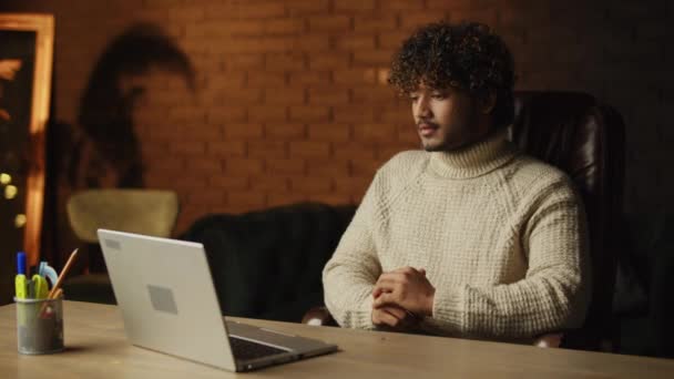 ビデオ通話をしているセーターのハンサムな若い男 オンライン会議中に慎重に聞いてノートパソコンを持つカーリー男 自宅の事務所で働いてる 高品質4K映像 — ストック動画