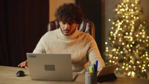 クリスマスにラップトップとデジタルテーブルを使用してフリーランス 休日に残業する若い男に焦点を当てた リモートジョブ 家庭からの仕事 高品質4K映像 — ストック動画