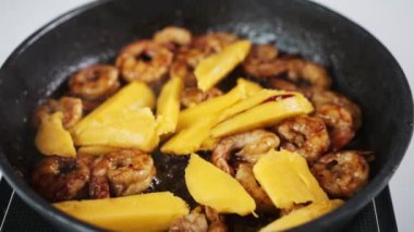 Cooking process of seafood. Slow motion footage of fruit pieces falling on the frying pan with shrimps. Delicious crusty prawns recipe. Chef making signature dish. High quality FullHD footage
