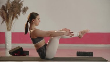 Fitness girl doing balance exercise on the sport mat. Side view of young woman stretching during home training. Beautiful sportswoman practicing yoga in her room. High quality 4k footage