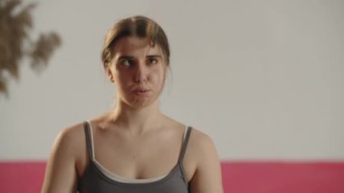 Tired young woman breathes heavily after training and taking hair away from her face. Front view of a girl in sport bra looking to camera. High quality 4k footage