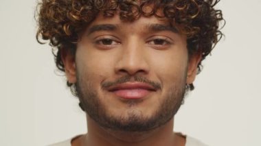 Handsome young man starts to laugh and closes his eyes. Curly mixed male model posing on white background in a good mood. High quality 4k footage