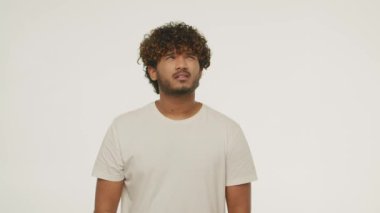 Confused brunette man posing in studio. Front view of bewildered guy rubbing his beard isolated on white background. High quality 4k footage