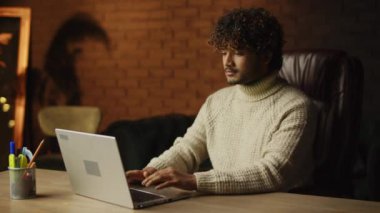 Concentrated freelancer is typing on laptop keyboard at home office. Indoor footage of focused young man working with computer in his room. High quality 4k footage
