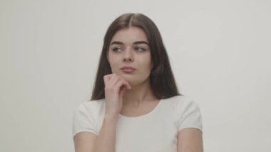 Beautiful girl looks thoughtfully into the camera trying to figure out how to solve the problem. Young brunette woman with a thoughtful look. Pensive lady propping her face with a hand isolated on