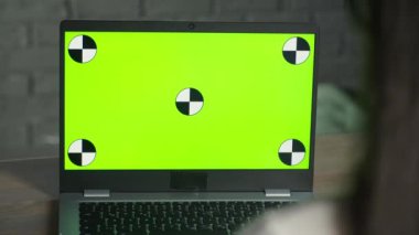 Kız stüdyoda otururken dizüstü bilgisayarında krom anahtarla çalışıyor. Uzaktan kumandalı bir bilgisayar. Yeşil ekran kavramı. Yüksek kalite 4k görüntü