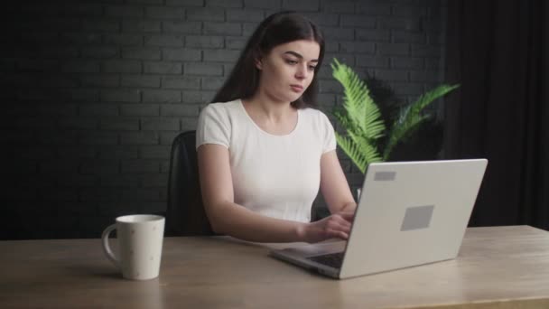 女自由撰稿人坐在演播室里 一边喝着一杯咖啡 一边勤奋地在她的笔记本电脑上打字 年轻的黑发女人在一个遥远的工作 专注于电脑工作的女孩 高质量的4K镜头 — 图库视频影像