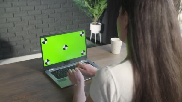 一个坐在桌旁的黑发女孩开始在带有绿色屏幕的笔记本电脑上工作 一个女人在电脑键盘上打字和看色键的背景图 在线学习 远程教育 — 图库视频影像