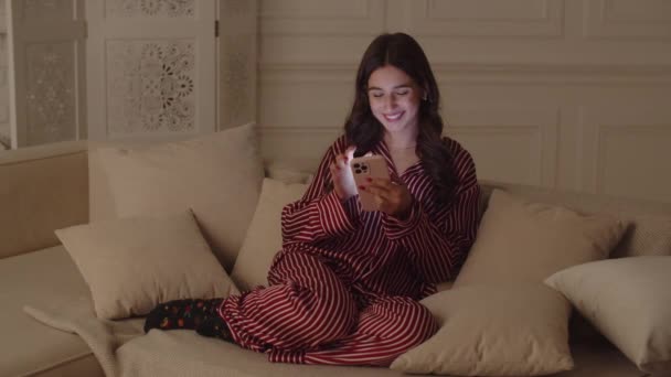 Woman Homemade Striped Pajamas Using Phone While Sitting White Sofa — Stock video