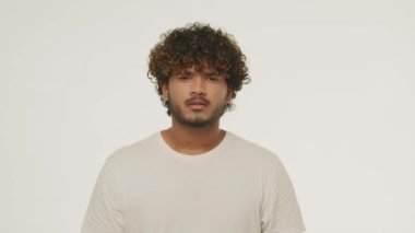 Curly young man showing mind explosion gesture. Front view of curly guy overwhelmed with news. Shocked male model gesturing on white background. High quality 4k footage