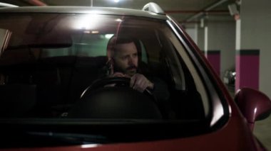 Angry man shouts on the phone at the parking lot. Mad driver making a call while holding car wheel. Negative emotions, bad mood. High quality 4k footage