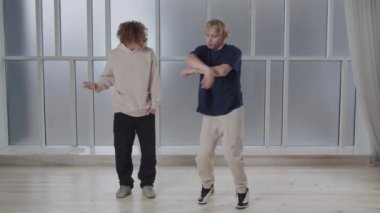 Full length view of two young men showing modern choreography moves. Contemporary dance in studio. Dance battle idea. High quality 4k footage