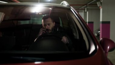 Esmer adam telefonda konuşuyor ve direksiyon başında. Şoför otoparkta arama yapıyor. Arabasında akıllı telefon kullanan meşgul bir adam. Yüksek kalite 4k görüntü