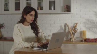 A young business lady is texting with her business partners and then pauses for a few seconds to think about the answer. Brunette freelancer girl working from home office. Distant job idea. High