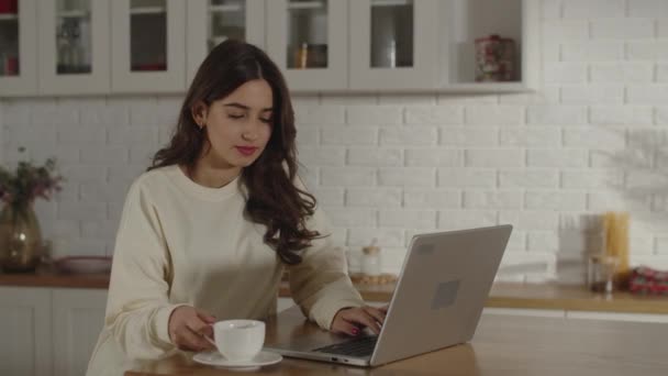 Female Freelancer White Sweater Works Her Laptop Drinks Coffee Brunette — Stockvideo