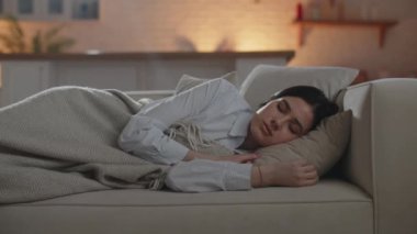 Attractive businesswoman taking a nap on the sofa. Brunette woman in shirt sleeping on the couch and covering herself with a blanket. High quality 4k footage