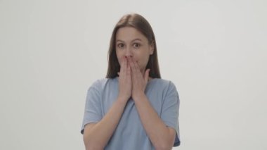 Video of a surprised brunette who covers her mouth with her hands. Shooting from the studio on a white background. High quality 4k footage