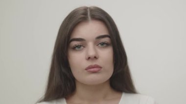 Close-up portrait of sad brunette girl. Front view of upset young woman looking at camera isolated on white background. High quality 4k footage