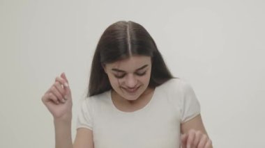 A brunette woman in a white t-shirt is dancing in front of the camera. Video of a young woman dancing against a white wall. High quality 4k footage