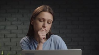 A female freelancer thinks about the details of a working project and then starts working on a laptop. Remote work at the computer from the studio. High quality 4k footage