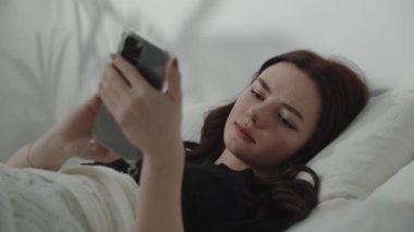 Güzel kız uyumadan önce biriyle sohbet ediyor. Çekici genç kadın mesajlarını gülümseyerek kontrol ediyor, esniyor ve uykuya dalıyor. Yüksek kalite 4k görüntü