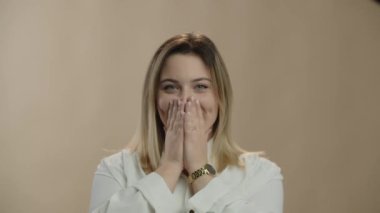 Excited blonde girl covering her mouth with hands. Cheerful young woman smiling when hearing good news. High quality 4k footage