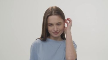 Video with a cute girl who smiles at the camera and hides her hair behind her ear. Portrait shooting of a girl in the studio. High quality 4k footage