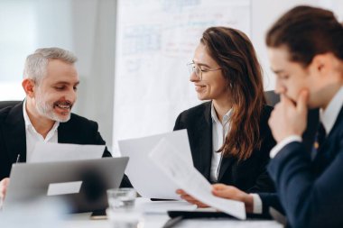 Business analytics with documents discussing new ideas. Smiling ceo talking with coworkers during office meeting. High quality photo