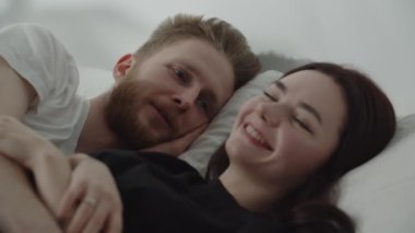 Waking up in the morning, a young couple lying in bed discussing plans for the day. Husband and wife come up with activities for t. High quality 4k footage