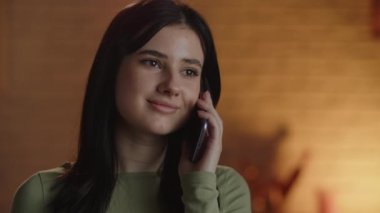Close-up of a young woman talking on the phone. Attractive brunette girl calling someone. Footage of beautiful female model using smartphone on blurred background. High quality 4k footage