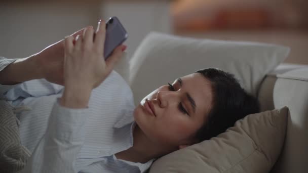Молодая Сонная Женщина Прокручивает Экране Смартфона Брюнетка Лежащая Диване Пролистывает — стоковое видео