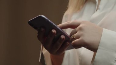 Cropped view of smartphone user. Woman with rings typing a message on the phone screen. Girl in white shirt browsing on mobile internet. High quality 4k footage