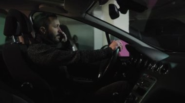 Nervous driver talking on the phone at the parking lot and gesturing emotionally. Side view of a man sitting in the car and making a phone. Stressed guy talking in auto. High quality 4k footage