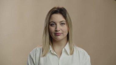 Beautiful blonde woman in shirt looking at camera. Studio portrait of attractive european girl with gentle smile. Front view of stylish female model. Natural beauty. High quality 4k footage