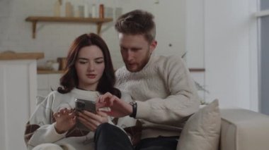 Young couple using smartphone together. Beautiful brunette girl shows her phone screen to boyfriend. High quality 4k footage
