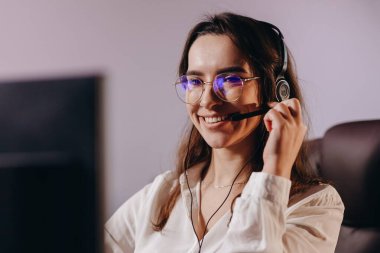 Hotline operator in headset looking at the computer screen. Smiling support agent girl at her workplace. Portrait of happy female call center worker. High quality photo