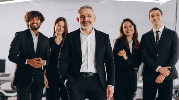 Smiling company executive with his team. Front view of laughing businesspeople in black suit posing together. Group of happy managers. High quality photo