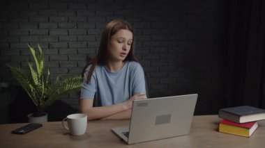 A tired woman sits at a table with a laptop and discusses a study project with classmates. Video with a woman who communicates with classmates via video link. High quality 4k footage