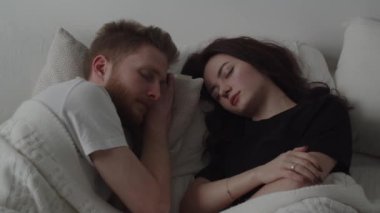Married couple sleeping in bed next to each other. Video of young woman and man taking a nap under blanket. High quality 4k footage