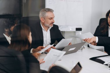 Colleagues discussing analytical report in the office. Coworkers reading documents during business meeting. High quality photo