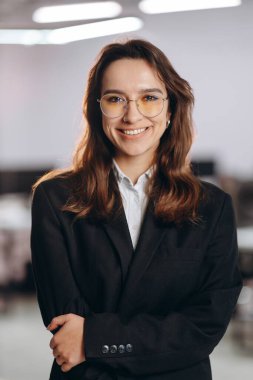 Confident businesswoman in glasses smiling on blurred background. Front view of female company ceo posing in office. High quality photo