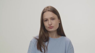 A brown-eyed woman standing against a white wall looks intently into the camera. Closeup shot of a beautiful brunette woman. High quality 4k footage