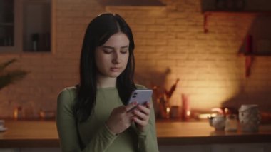 A dark-haired woman quickly types something on her smartphone. A brunette girl is focused on writing a reply to a message. Female model with phone browsing internet. High quality 4k footage