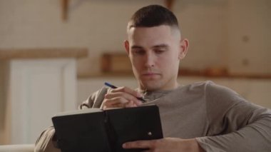A young man with a short haircut makes notes in his notebook. Businessman makes a to-do list for tomorrow. Focused guy writing his diary. High quality 4k footage