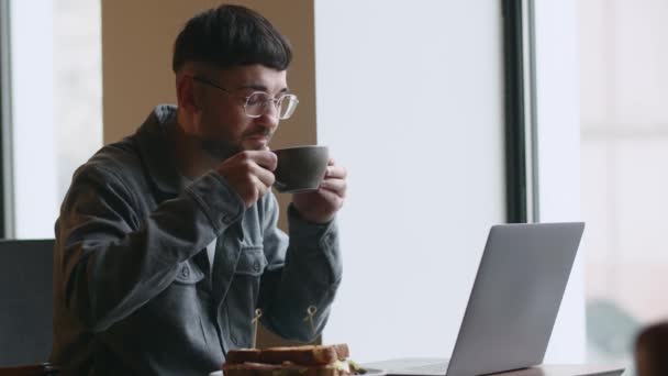 카페테리아에서 일하는 프리랜서는 커피를 마신다 하우스 노트북으로 안경을 남자를 있습니다 — 비디오