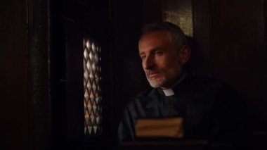 Pastor listening to someones confession in confessional booth and nodding with understanding. Catholic priest listens to anonymous sins confession. High quality 4k footage